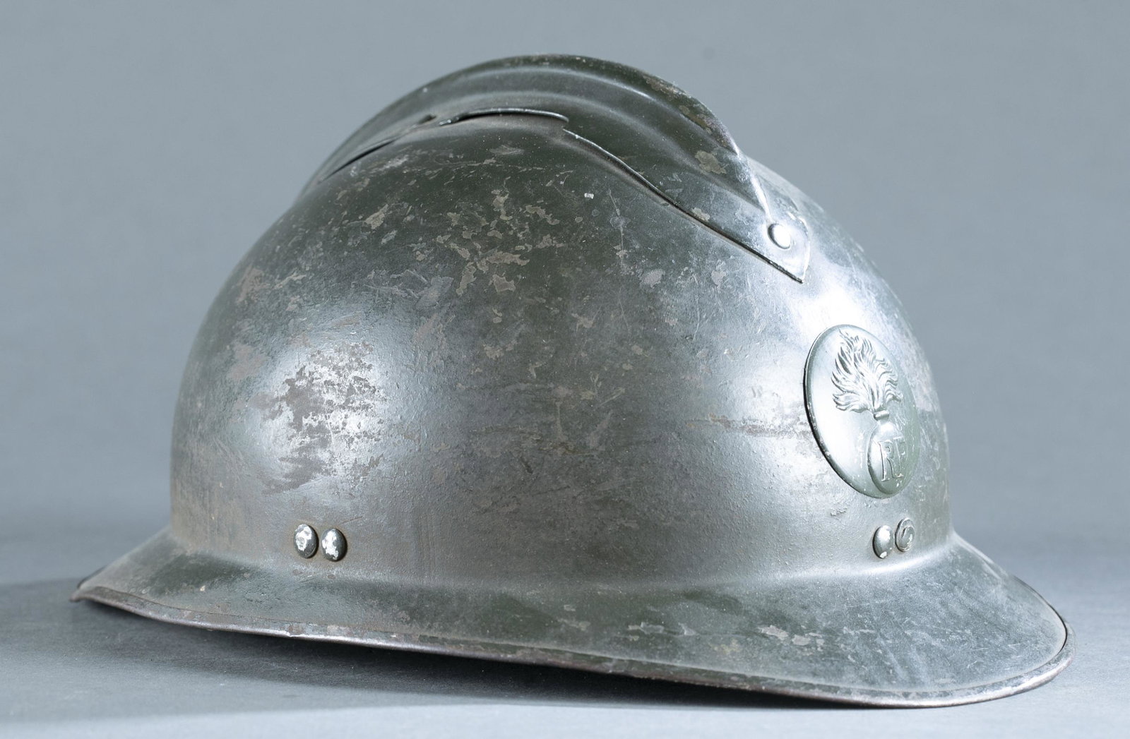 WW2 French M26 infantry Adrian helmet.: WW2 French M26 infantry Adrian helmet. Includes original liner and chinstrap. Flaming bomb with RF infantry insignia in front. 7" x 12 1/2" x 9 1/8". Condition: 60% of original paint. Wear on the outs