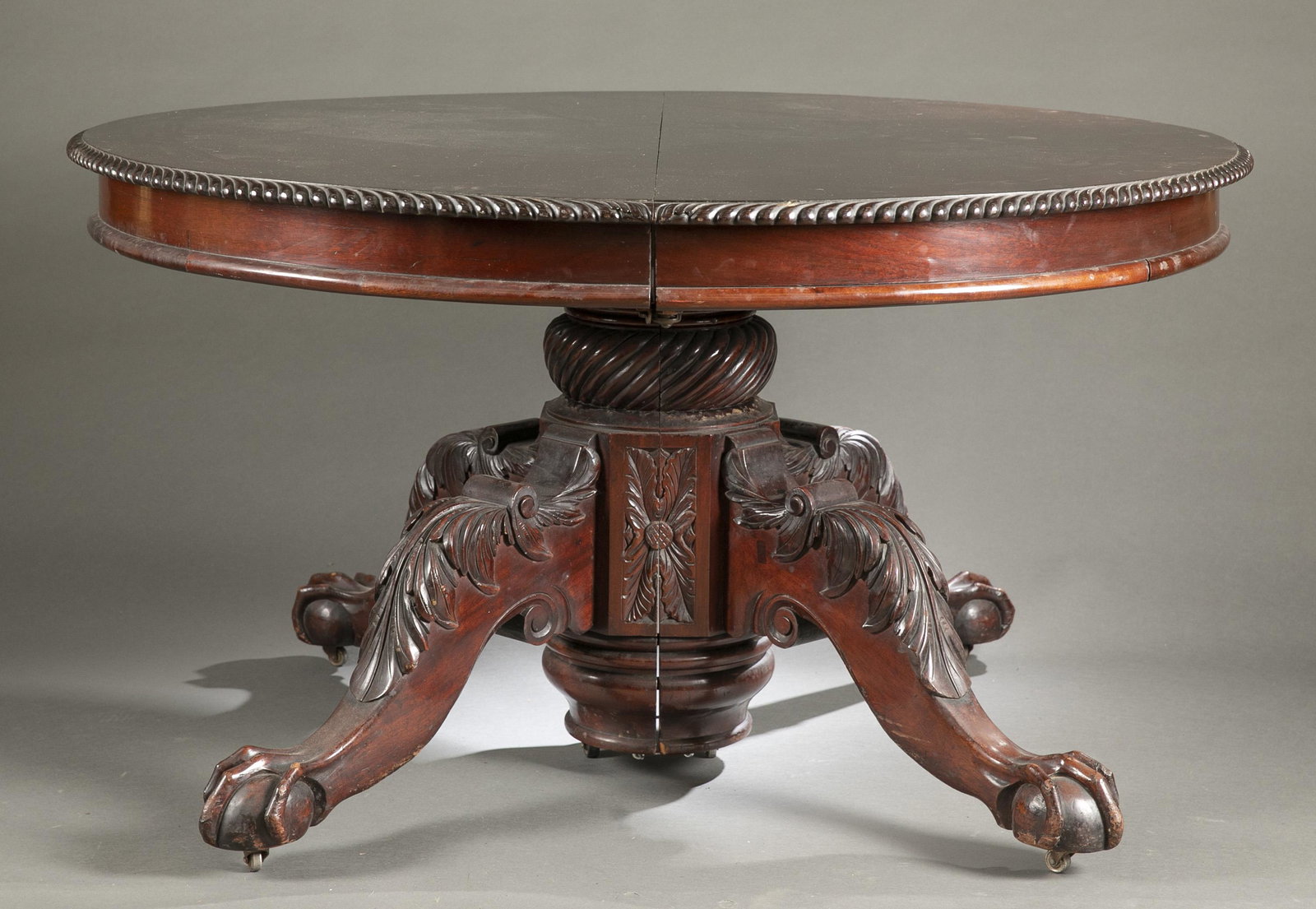 Claw and ball foot dining table: An Antique mahogany dining table, 20th century. Circular top with six legs with acanthus leaf decoration and claw and ball feet. Includes one leaf. 26" x 53"Provenance: From the Mike & Jean Clinton Fa