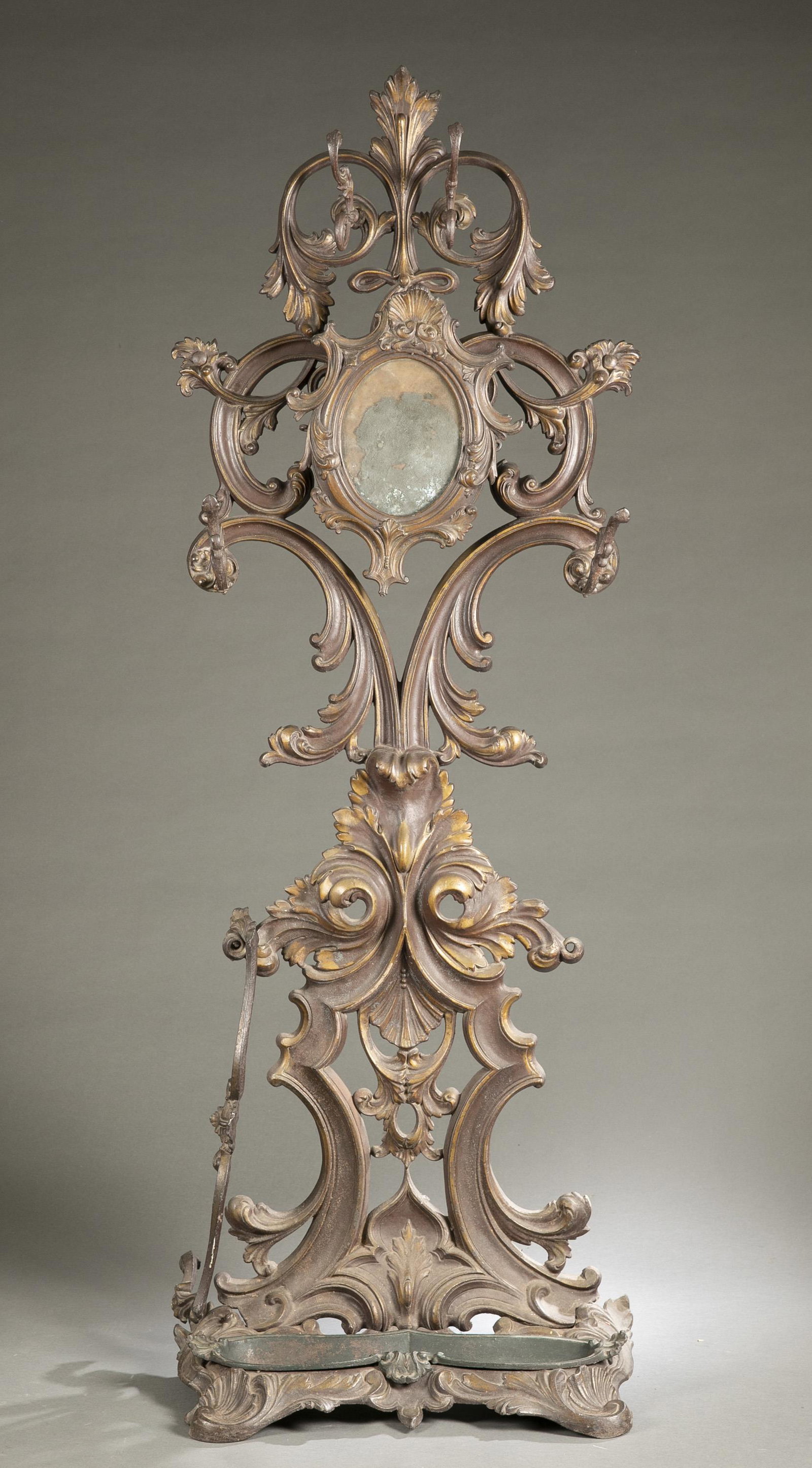 Rococo Revival John Moore cast iron hall tree.: A Rococo Revival John Moore rococo cast iron hall tree, 19th century. Rocaille form with six coat hooks with central adjustable mirror, over umbrella holder with removable tray. 75 1/2" x 25 1/2" x 13