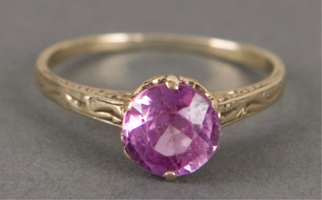 Gold solitaire ring with pink stone.: Solitaire ring in 14KT yellow gold with etched shoulders and intricate basket setting for single pink piece of glass or stone. Size 6