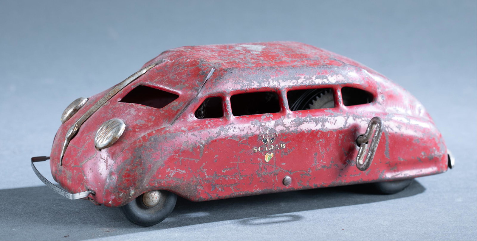 Buddy L Scarab pressed steel car.: A Buddy L Scarab pressed wind up steel car. Partial decal on each side.10 1/4" long.Condition: Non functional. Heavy wear and loss of paint. Rust on metal.