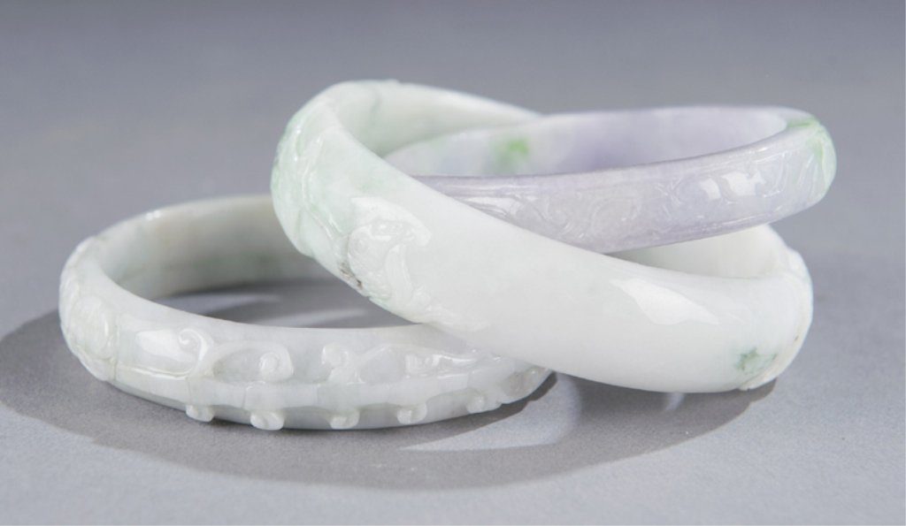 Group of three Chinese bangle bracelets w/ purple.: Group of three Chinese carved jade bangle bracelets. 20th century. With purple and darker green inclusions. Carved lingzhi and lotus pods. 2 1/2"diam., 2 3/4"diam., 3"diam. Condition: Good.
