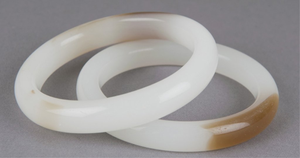 2 Chinese white and russet hard stone bangles.: Group of two Chinese white and russet jade or hard stone bangle bracelets. 20th century. 3 1/4"diam. Condition: Good.