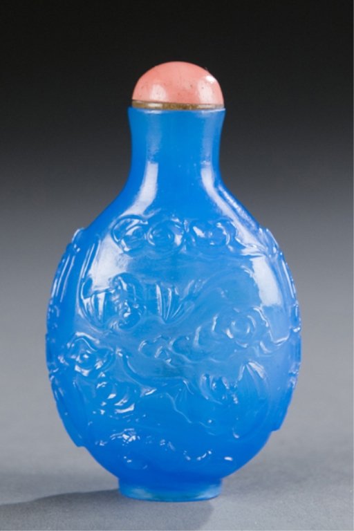 A Chinese blue glass snuff bottle, relief dragon.: A Chinese blue glass snuff bottle with relief dragon design. c.1850-1900. Flattened ovoid form with flaring neck. Faux coral stopper. 2 3/4". Provenance: From the Collection of John W. Sinclair, Calif