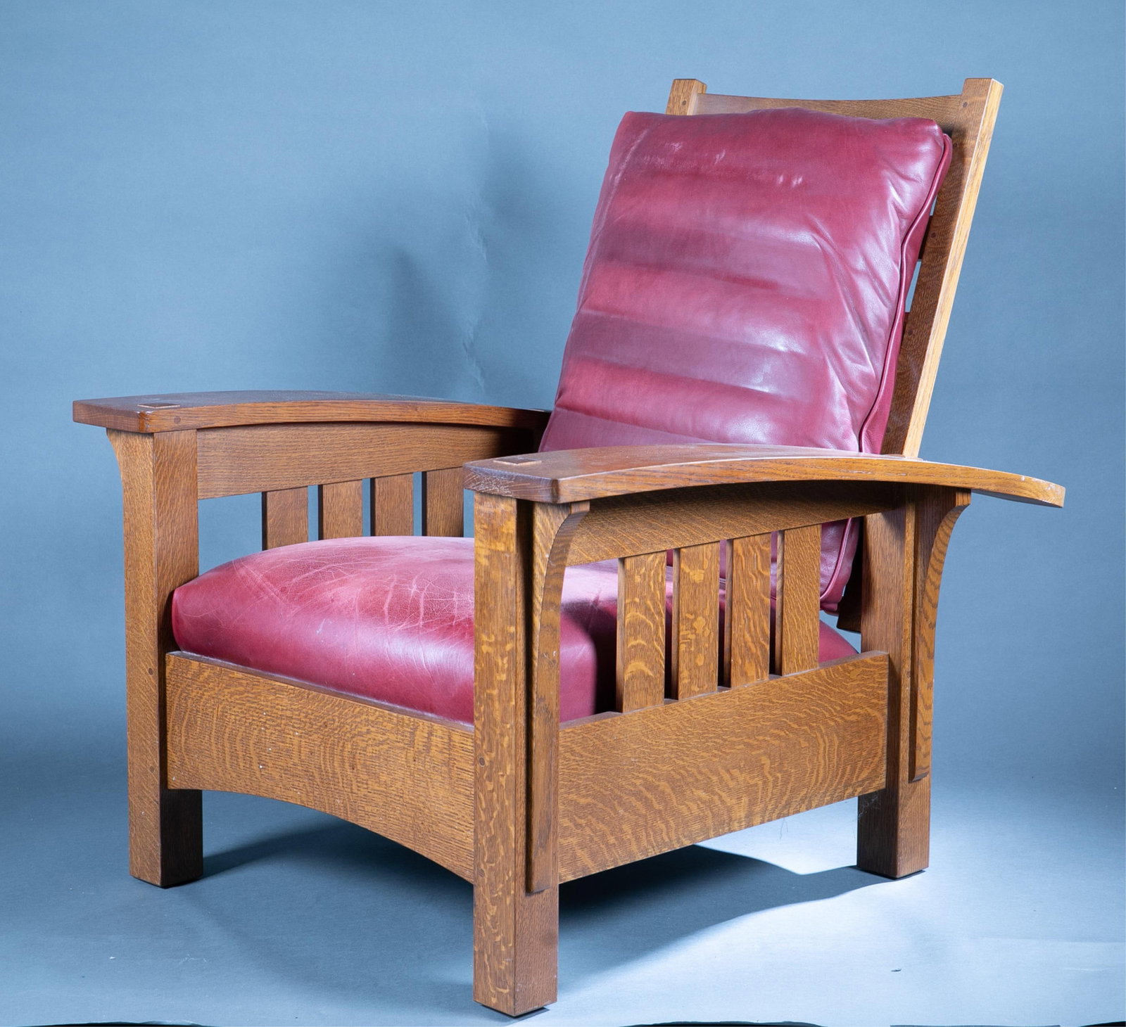 Stickley Bow Arm Morris Chair and stool: A Stickley Furniture oak Bow Arm Morris chair, 89-406, and matching footstool, 89-495, both with red leather upholstery. 21st century. Chair: 35" x 40" x 40"; footstool: 19" x 15" x 15".