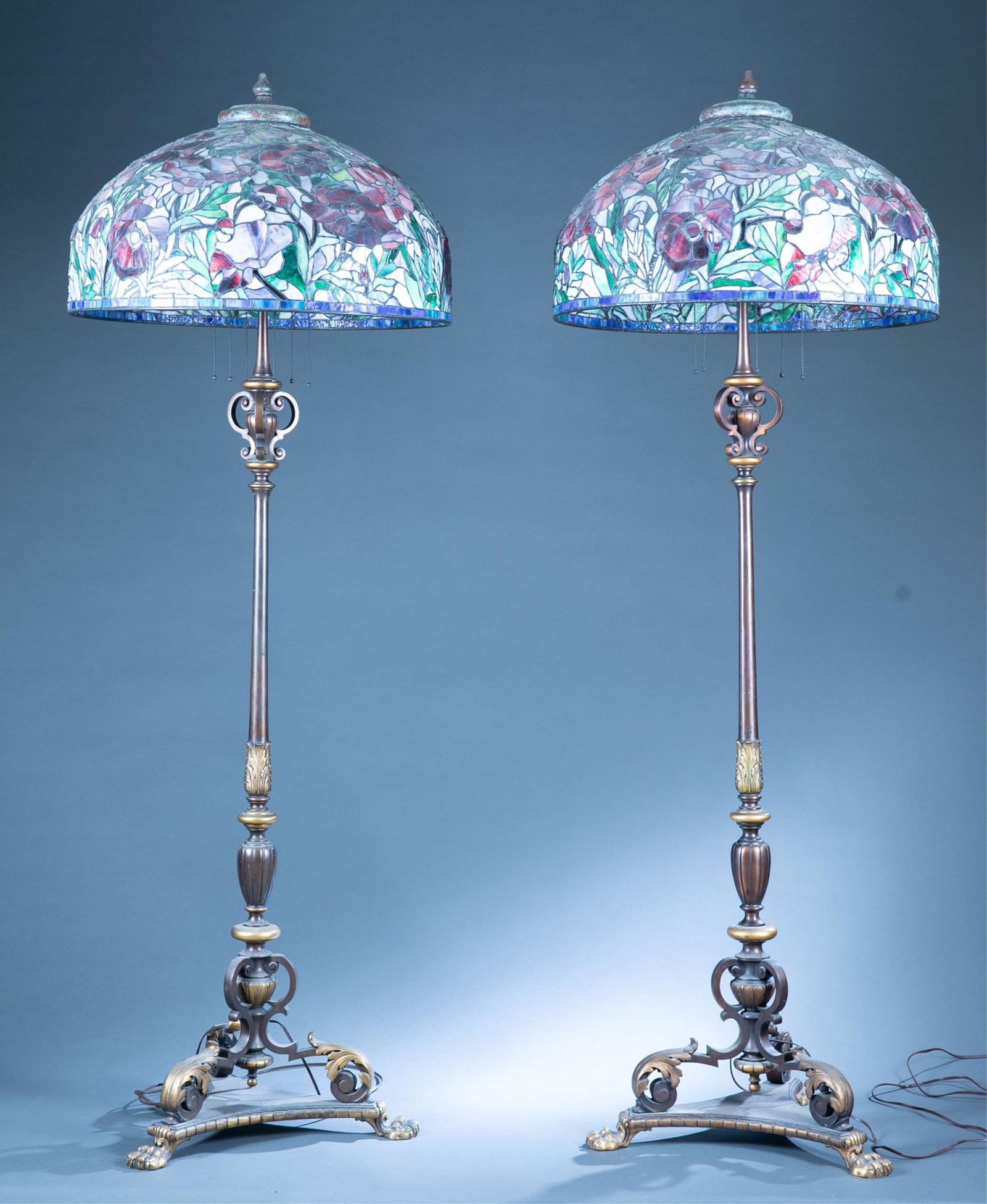 2 Tiffany Studios style standing lamps: A pair of Tiffany Studios style six light torchere neoclassical standing lamps, Early 20th Century. Incorrectly marked on base "TIFFANY & CO." Floral leaded glass shade by Ray Folio of Folio Art Studi