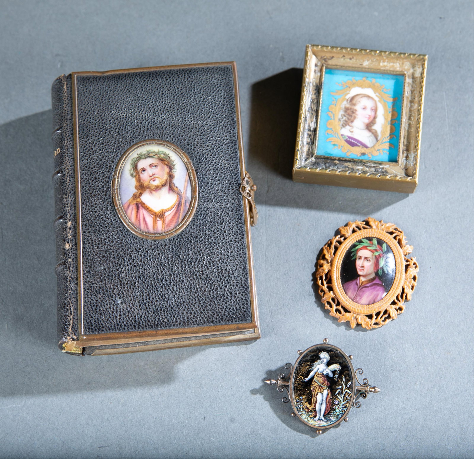 Group of portrait miniatures: A group of portrait miniature items. Including a miniature prayer book with a latch and depiction of Jesus with the thorn crown on the front, pin with a depiction of Demeter, portrait of Dante in a ca