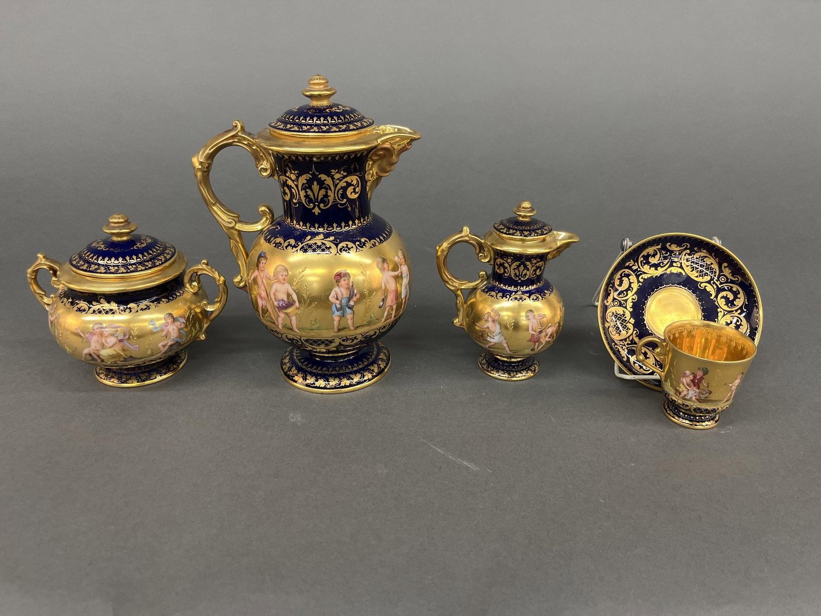 Royal Vienna marked cobalt tea set: A Royal Vienna marked tea set. Cobalt and gilt design with frieze of putti and cupids. Signed "Ullmer." Marked with variations of underglaze shield/ beehive mark and labeled Winter, Toast, Fanfare, Si