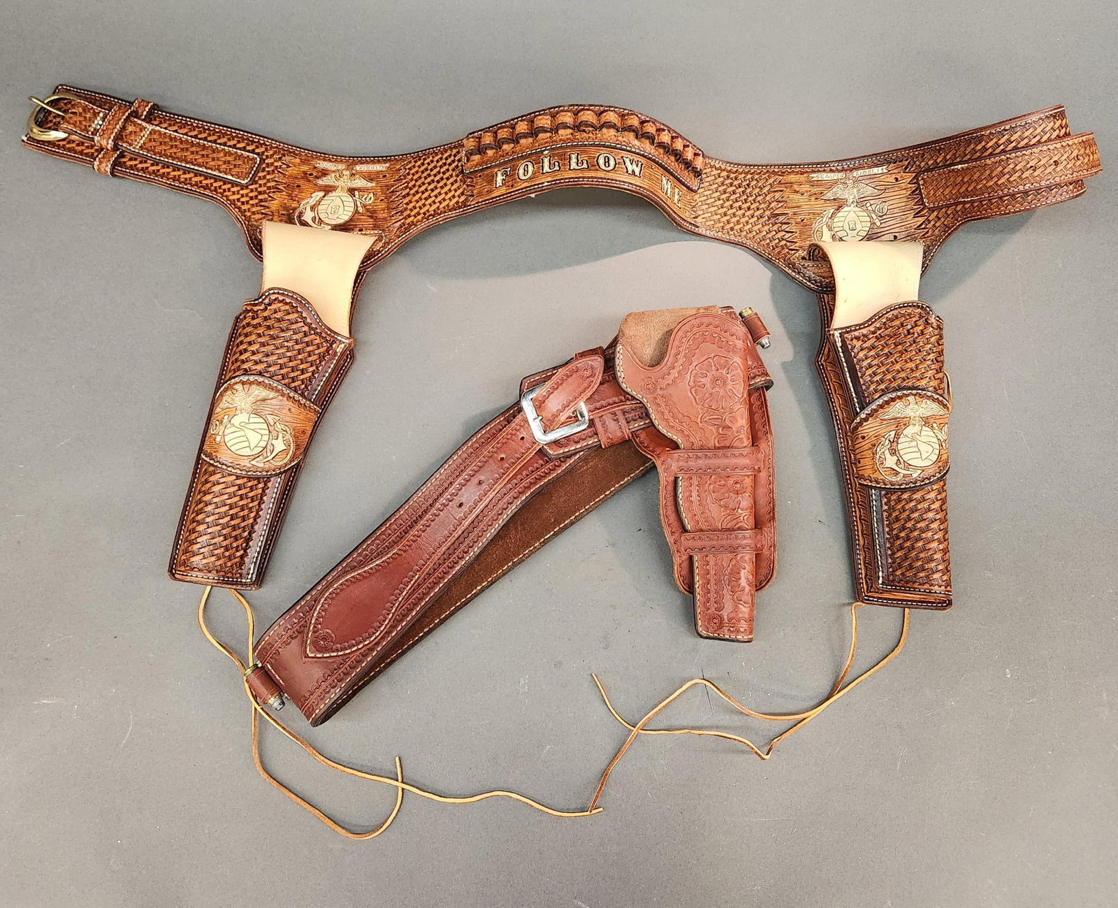 2 Tooled leather revolver holsters: A group of two tooled leather revolver holsters. USMC two revolver holster. U.S.M.C. emblem on both side and on holsters and "FOLLOW ME" on reverse of belt. ++ One revolver holster with cartridge belt