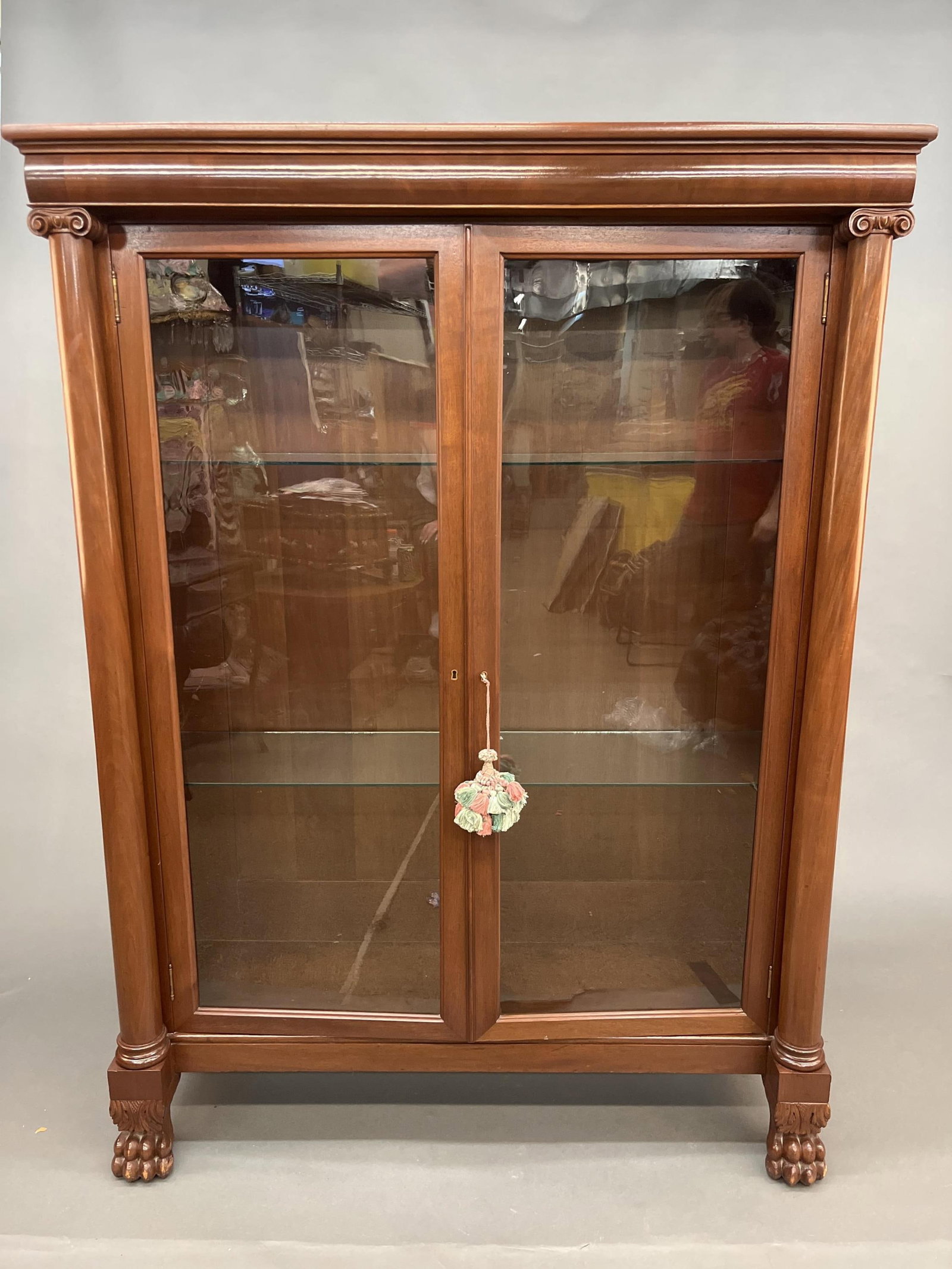 Neoclassical walnut display cabinet: A Neoclassical walnut display cabinet. Glass door revealing two shelves flanked by ionic capital columns and raised on claw feet. 66 1/4" x 49" x 16 1/2". Provenance: From the estate of U.S.M.C. Four 