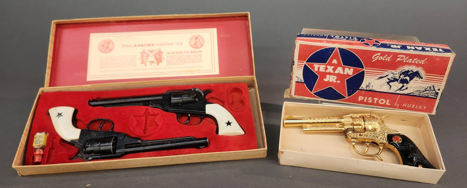 2 Vintage toy guns in box: A group of two vintage toy guns in box. ++ B.C.M. Co. (Derby) Ltd the Apache calibre .44. Missing badge. 1 1/2" x 15 1/2" x 6" ++ Hubley A Texan Jr. gold plated pistol. 1 1/2" x 9 1/4" x 4 1/4"