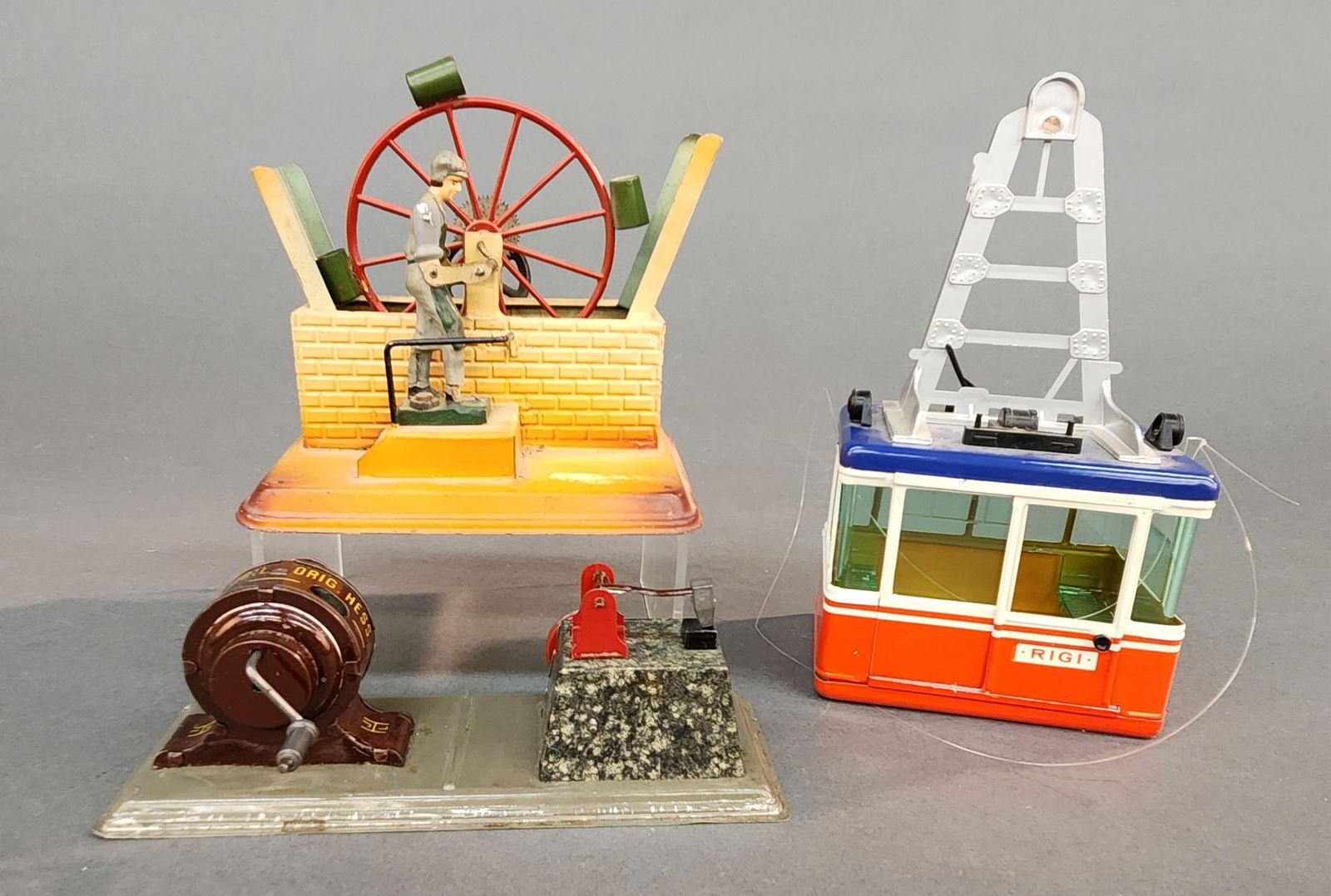3 German toys: A group of two German toys. ++ Fleischmann hand powered water wheel with composition figure. 5 1/2" x 6" x 4" ++ Hess Dynamobil with trip hammer. 2 1/2" x7" x 2 1/2" ++ Lehmann Rigi Duo cable railway