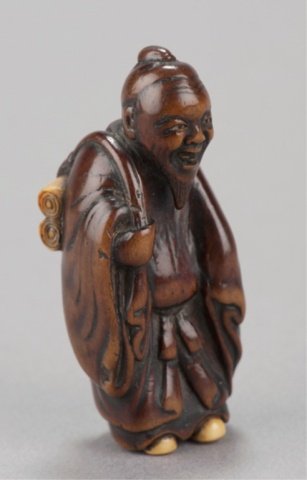 ,A wood netsuke of a Chinese scholar.: By Hidemasa I, Kyoto/Tokyo, Early 19th century. Standing and carrying two scrolls on his back. The scrolls, and his feet are of ivory and his eyes are ivory with black pupils. The ivory on the scrolls