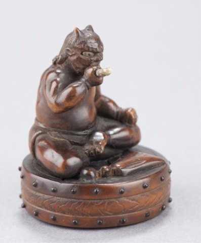 A wood netsuke of Oni on drum.: By Gyokushi, Early 19th century. Sitting cross-legged atop a taiko drum, smoking a pipe which is made of bone, his eyes are double-inlaid in antelope horn with black pupils, the two rows of beads that