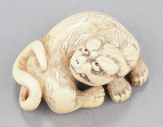 An ivory netsuke of a tiger.: Mid 18th century. Reclining with head slightly raised, eyes inlaid in black, the body gracefully twisted as he turns his head to the right, the hair-work well-worn and the stripes carved as reserves f