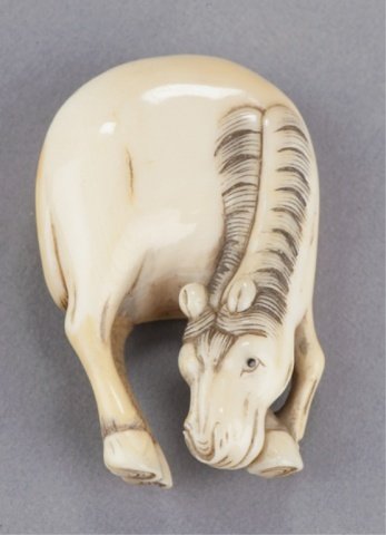 An ivory netsuke of a horse.: Mid 19th century. Grazing, the eyes inlaid in black, the tail curled around the back just below the large himotoshi of unequal size, gentle wear and some patination on the back. Unsigned. 2in (4.9cm).
