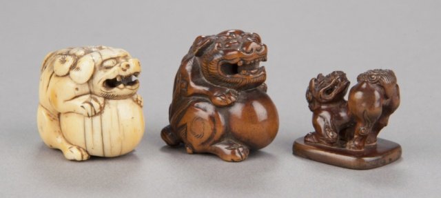 A group of three Shishi netsuke.: Mid 19th century. The first, in ivory, seated with mouth open and all four legs wrapped around a large tama. 1 1/4in (3cm). The second, in wood clutching a large tama, a loose ball in its mouth, a thi
