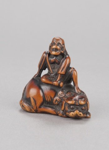 A wood netsuke of a Sennin on a shishi.: Mid 18th century. Seated atop the shishi, with a gourd. Unsigned. There is a nearly identical piece, also unsigned, in the Behrens Collection, No. 4316 and illustrated on Plate LV. Joly describes that