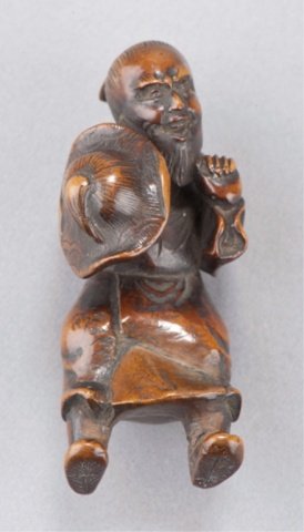 A wood netsuke of a Mongolian man.: Late 18th century. Standing but slightly stooped over, his clenched left hand raised in front of him, he holds a large hat with a wide curled brim in his right, some wear and the right foot has been r