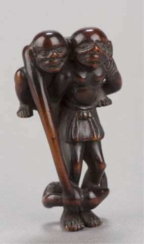 A wood netsuke of Ashinaga and Tenaga.: Late 18th century. Tenaga on Asinaga's back leaning down to grasp an eel that has wrapped itself around Ashinaga's legs, dark wood with a good patina.2 7/8in (7.3cm). Provenance: Behrens collection, N