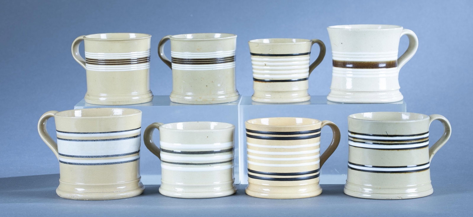 8 Yellowware mugs: A group of eight yellowware ceramic mugs. Each with multiple white and brown band decoration. Largest: 3 7/8" Smallest: 3" Condition: Crazing, Condition consistent with age and use.