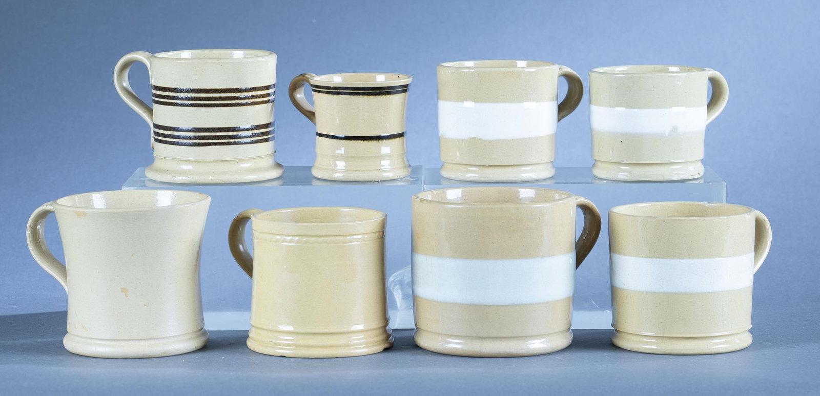 8 Yellowware mugs: A group of eight yellowware mugs. Largest: 4" Smallest: 2 3/4" ++Four with large white band decoration.++Two with brown band decoration. ++Two blank, one concave and one rouletted. Condition: crazing,