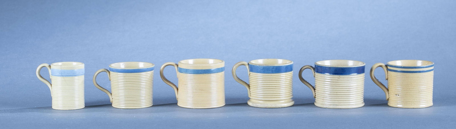 6 Yellowware mugs: A group of six yellowware miniature mugs. Each with blue bands and ridged sides. 2" Condition: crazing
