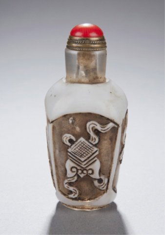 White glass snuff bottle. Late 19th/early 20thC.: A glass snuff bottle with four panels in single white overlay. Late 19th/early 20th century. Each panel with a scholars items. Sitting on a raised foot with a red coral top and brass spoon. 2 1/2"h.