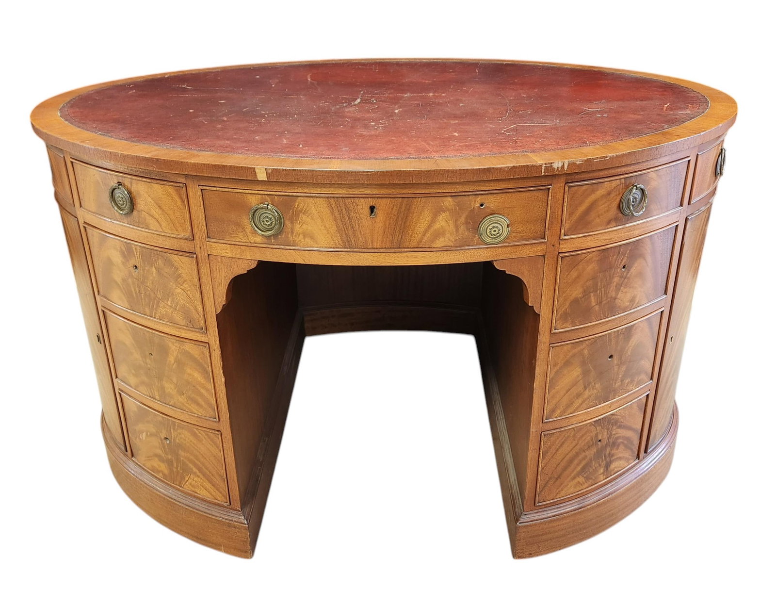 Oval leather topped kneehole desk.: An oval leather topped kneehole desk. 19th century. Nine drawers on front, six missing pulls, and flanked by two doors on side revealing shelf. 30 1/4" x 50 1/4" x 35".