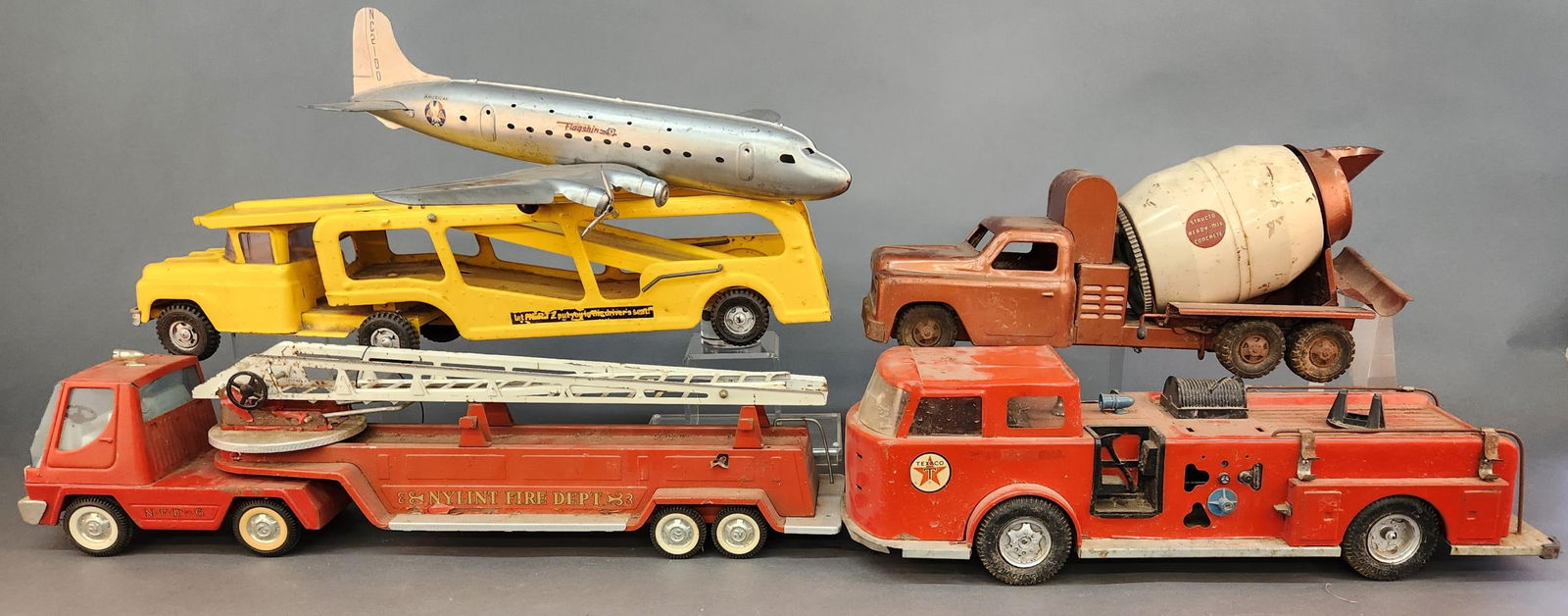 5 Vintage pressed steel vehicles: A group of five vintage pressed steel vehicles. Including Buddy L Hertz car carrier, Structo Toys cement Mixer, Nylint Toys ladder truck, Buddy L Texaco fire engine, and Marx, and Marx AA American
