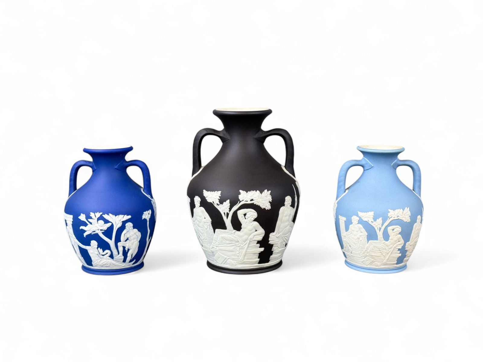 3 Wedgwood Jasperware Portland vases, 1892-1908.: A group of three blue and black Wedgwood Jasperware Portland vases. Circa 1892 to 1908. Marked "WEDGWOOD" and "England" on bottom. Smallest: 6" x 4 1/2". Largest: 8" x 6". Condition: Surface dirt, res