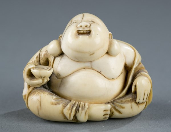Carved ivory netsuke of seated Buddha with bowl: A carved ivory netsuke of a seated smiling Buddha holding a bowl. Late 19th/early 20th century. Signed underneath. 1 3/4"h x 2"w.