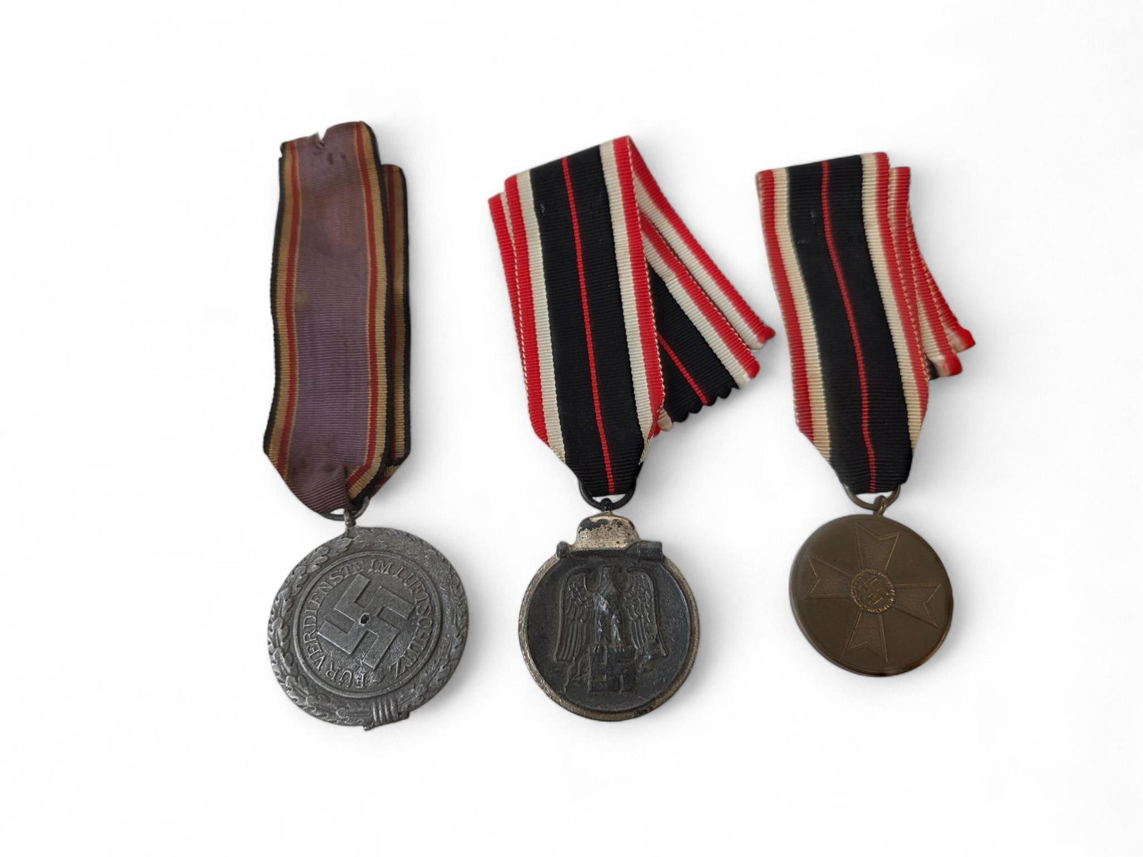 3 WWII German medals: WWII German War Merit Medal, Eastern Medal, Civil Defense Decoration 2nd Class medals. Condition: All cut ribbons. Civil Defense Decoration ribbon stained and has hole in center.