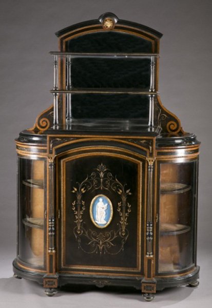 Two tier display case of ebonized wood w/ glass: A tall ebonizedand inlaid cabinet. 19th century. Base with central large door with plaque, flanked by reeded columns which are flanked by curved glass doors revealing cabinets with glass shelves. Narr