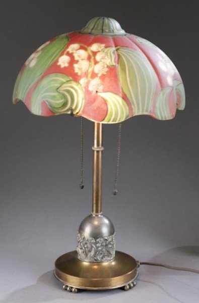 Pairpoint reverse painted table lamp lily: A Pairpoint reverse painted table lamp. 20th century. Red background with white Lily of the Valley and green leaves, exterior accented with black and gold lines. Metal base with 4-arm support and 2 fi