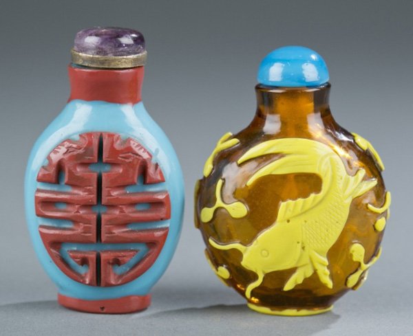 Group of 2 Chinese Glass Overlay Snuff Bottles: A group of two Chinese glass overlay snuff bottles. 19th/20th century. ++ Yellow on amber with fish and a blue acrylic top. 2" h. ++ Cinnabar on blue with a purple glass top and gold collar. 2 1/8" h.