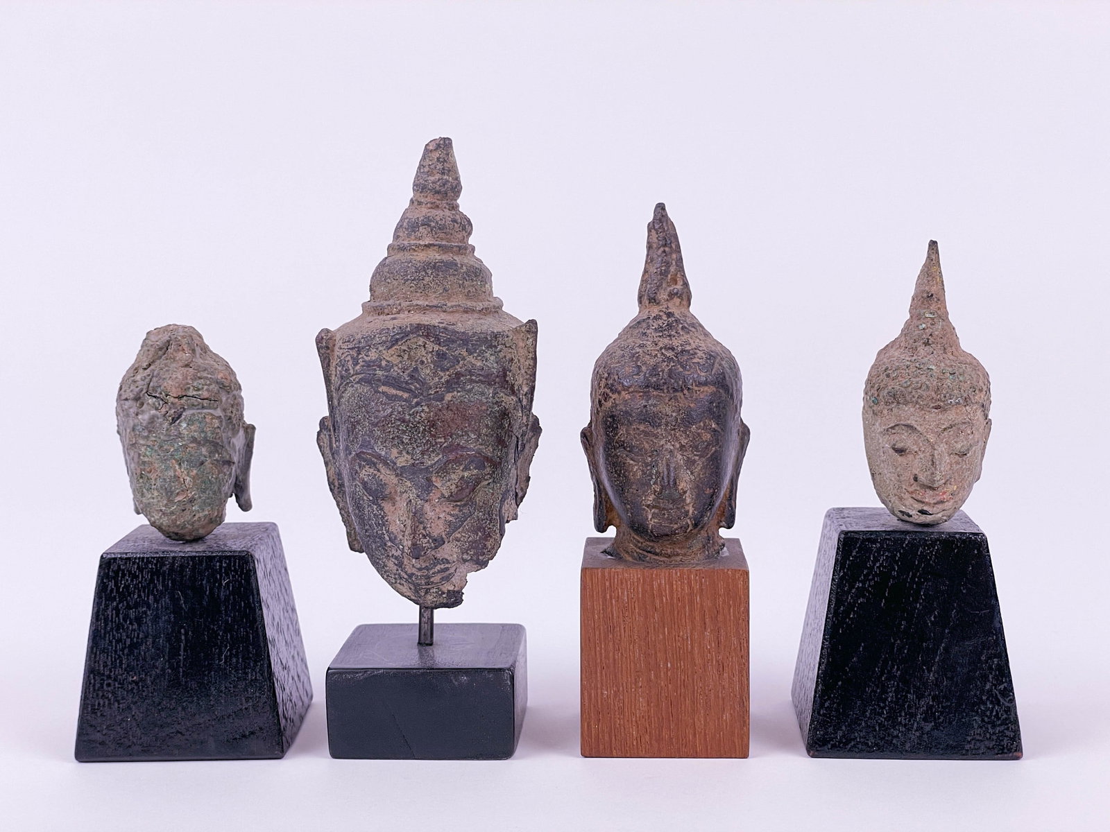 4 South East Asian Buddha heads.: Group of four Southeast Asian Buddha heads, comprising three carved stone examples and one bronze example, likely from Thailand or neighboring regions. The group includes heads of varying scale and st