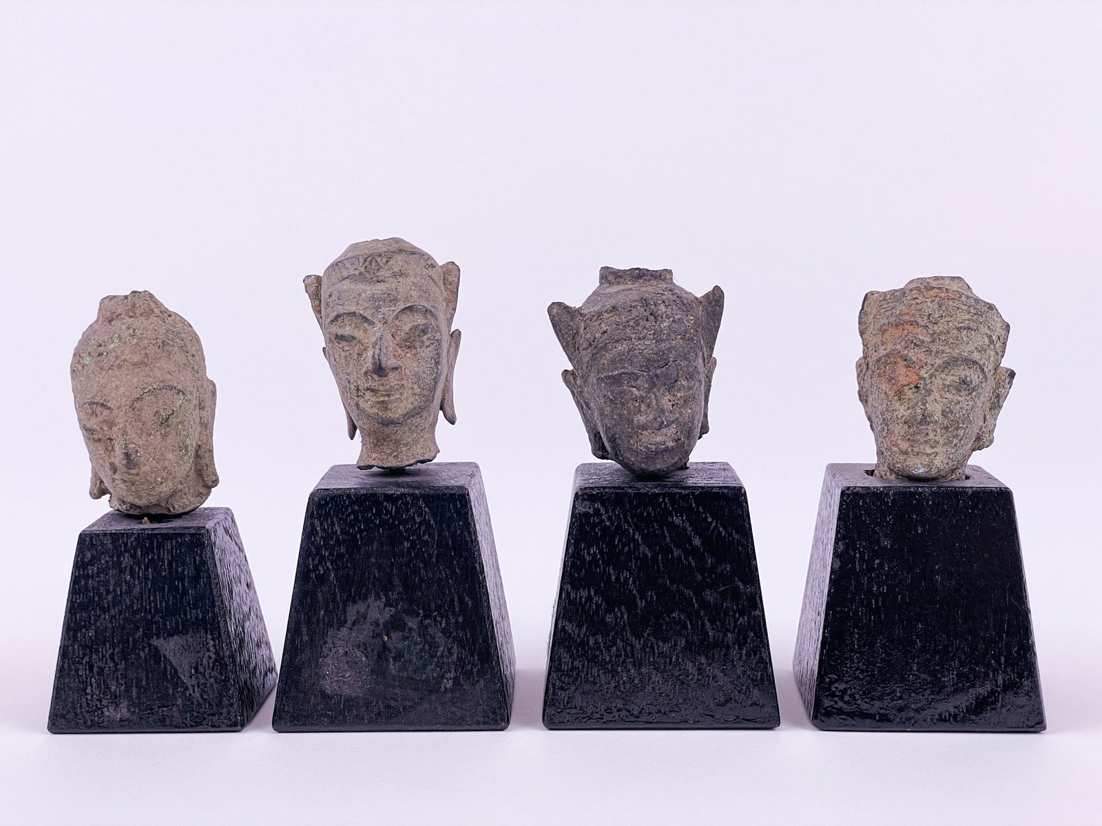 4 Buddha heads.: A group of four metal Buddha heads. Smallest with mount: 3 1/4" x 1 1/2". Largest with mount: 3 5/8" x 1 3/4". Condition: Abrasions, loss, and cracks.