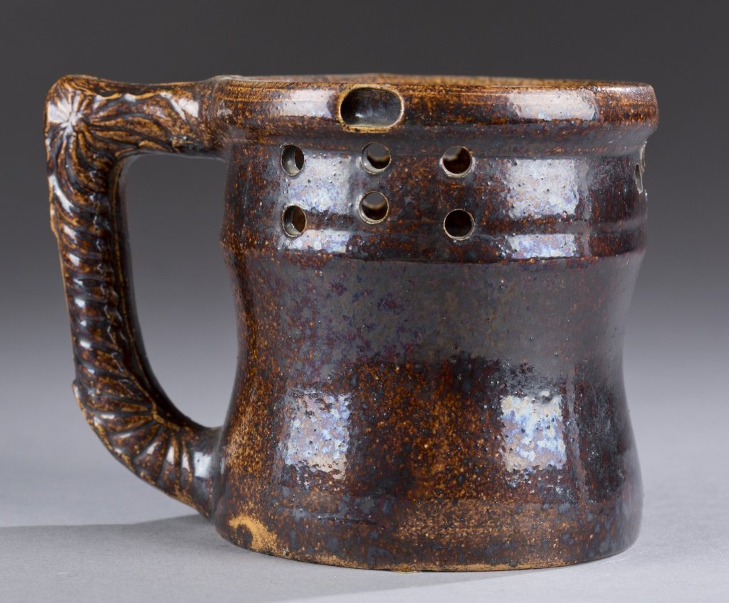 A George Ohr puzzle mug. Brown glaze. Signed on bottom: A George Ohr puzzle mug. Brown glaze. Signed on bottom in script, G.E. Ohr. 3 3/4"h x 3 5/8"diam.
