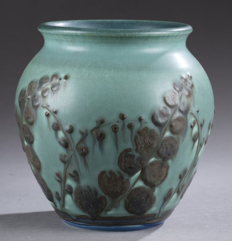 A Rookwood vase by Elizabeth Barrett. 1929. Green: A Rookwood vase by Elizabeth Barrett. 1929. Green foliate stalk design raised and layered on blue background. Impressed on bottom, Rookwood symbol, XXIX, 130 and artist mark. 6 1/2".