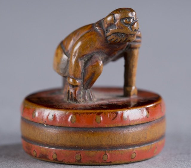Japanese red lacquer netsuke of an oni on a drum.: A Japanese red lacquer netsuke of an oni on a drum. Late 18th century. Carved wood with red and black lacquer. The Oni leaning on mallet having crawled out of hole in the drum. Himotoshi on the bottom