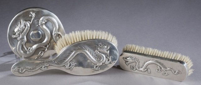 Chinese silver hand mirror and brushes.: A group of Chinese silver accessories. ++ A hair brush with the dragon in repousse. Marked on handle, "WH," for Wang Hing, 90. 9 1/2". ++ A hair brush with dragon in repousse. Marked on end, " WH," fo