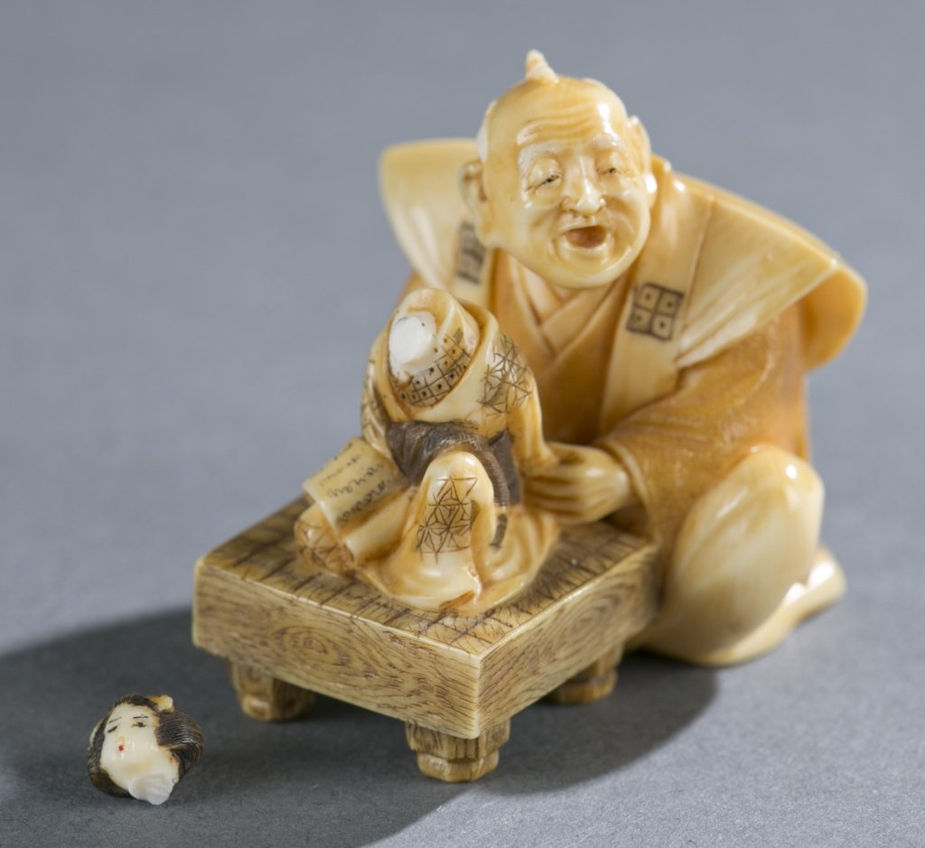 Japanese ivory netsuke of doll maker.: A Japanese ivory netsuke of doll maker, signed Gyokuzan. Mid 20th century. Seated man with doll on table. Himotoshi and signature in rectangular reserve on the bottom. Head of dollneeds to be re-attac