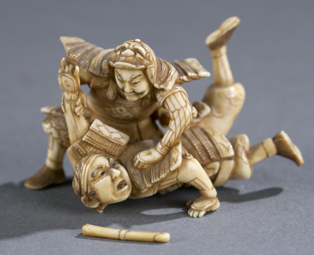 Japanese ivory netsuke of two samurai.: A Japanese ivory netsuke of two samurai, signed Hide Tsugu. Mid 19th century. Osaka school. One samurai is restraining other samurai who is on the ground. Himotoshi on the bottom, signature in red dye