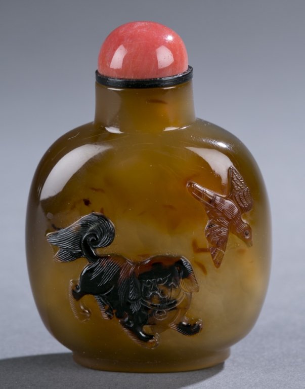 Chinese agate snuff bottle with relief carved: A Chinese agate snuff bottle with relief carved Buddhist lion. C.1750-1860. With 2 low relief carved birds. Rounded rectangular form, well hollowed. Having a pink stone cabochon with black collar stop