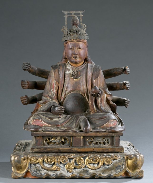 A Japanese wooden figure of goddess Benzaiten.: A wooden Japanese Buddhist goddess figure of Benzaiten.19th century. Red painted and gilded wood. Eight-arms variation of Benzaiten, sitting on a throne, with a torii and a figure on her head. Holding
