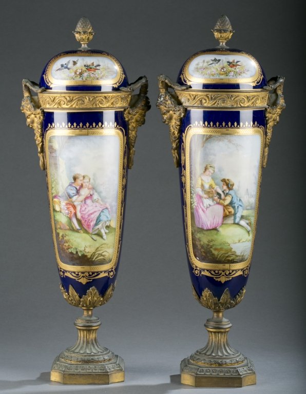 Pair of Sevres garniture urns in royal blue c1780.: A pair of Sevres garniture covered urns in royal blue with gilded inserts. Decoration includes a floral scene, a courting couple scene, gilded bronze satyr handles, acorn finials and feet. 17 3/4"h x 