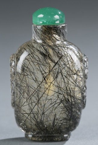Chinese black hair rutilated quartz snuff bottle.: A Chinese hair crystal snuff bottle. c.1820-1880. Rounded rectangular form, with mock mask and ring handles. On oval foot, with green glass stopper. Well hollowed. 2 3/8"h. Condition: A few natural mi
