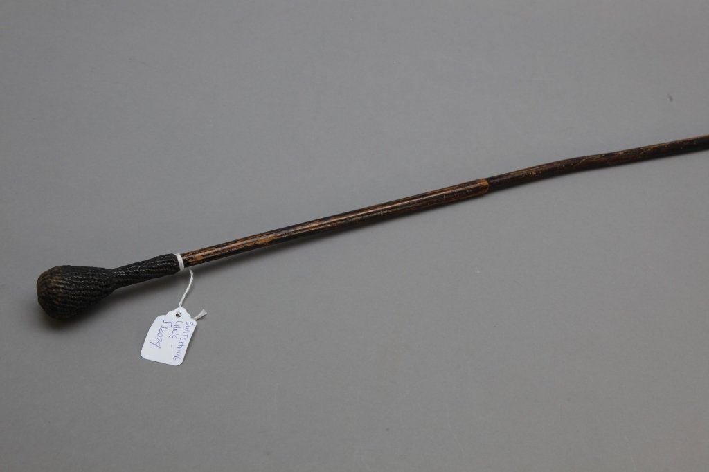 Rattan Cane or Switch with Handle: [Cane or Switch] A rattan cane or switch w/ carved or tooled attached head. Dark brown varnish or paint over flexible rattan palm stem, 33 3/4 in. long, apprx 1/2 in. wide, 3 1/2 in. handle or head w/
