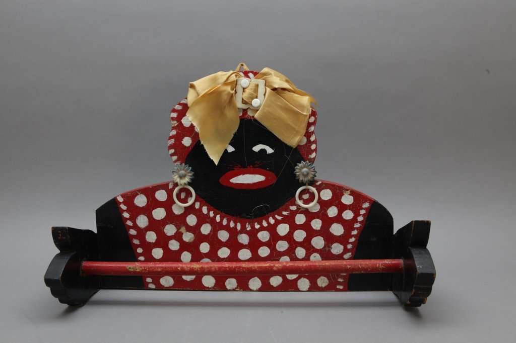 Black Folk Art Painted Mammy Towel Rack: [Folk Art Painted Towel Rack]. Early 20th C. elaborate painted and decorated "Mammy" towel bar or towel rack. Wooden board and bar w/ ribbon bandanna and flower earrings. Painted in red, black and whi